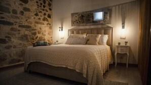 Ein Schlafzimmer mit einer Steinswand, einem Bett mit beiger Decke, zwei Nachttischen mit Lampen und einem Gemälde über dem Bett.