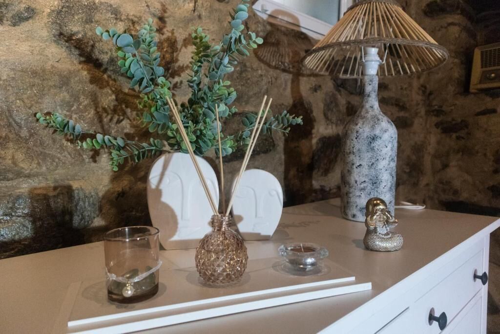 A table with a vase of green foliage, a glass candle holder, a decorative lamp, and a small figurine.