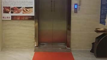 An elevator with a red carpet leading to it, a wall-mounted sign with text, and a digital display above the elevator door.