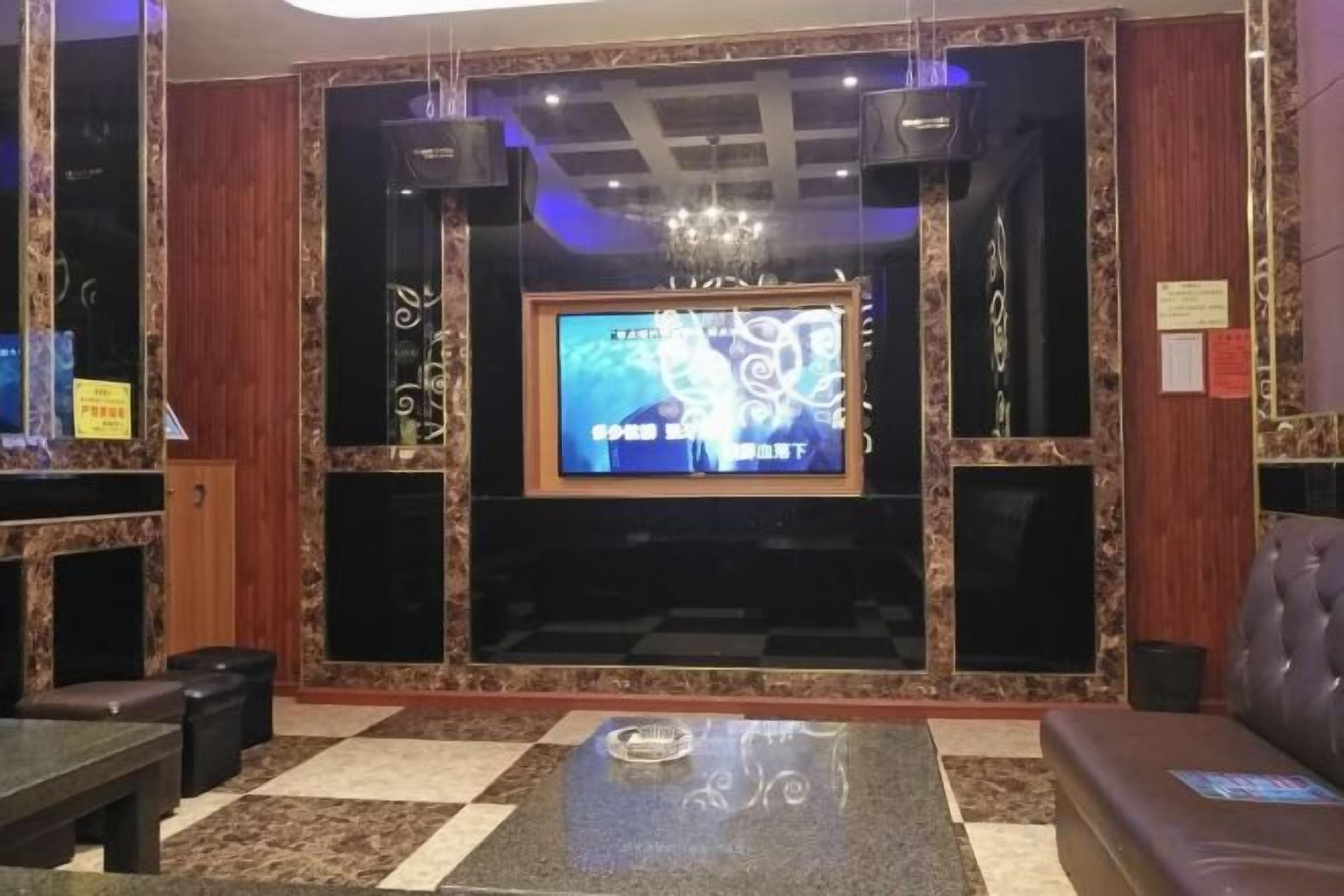 A hotel lobby with a checkered floor, a television screen, a chandelier, and a seating area.