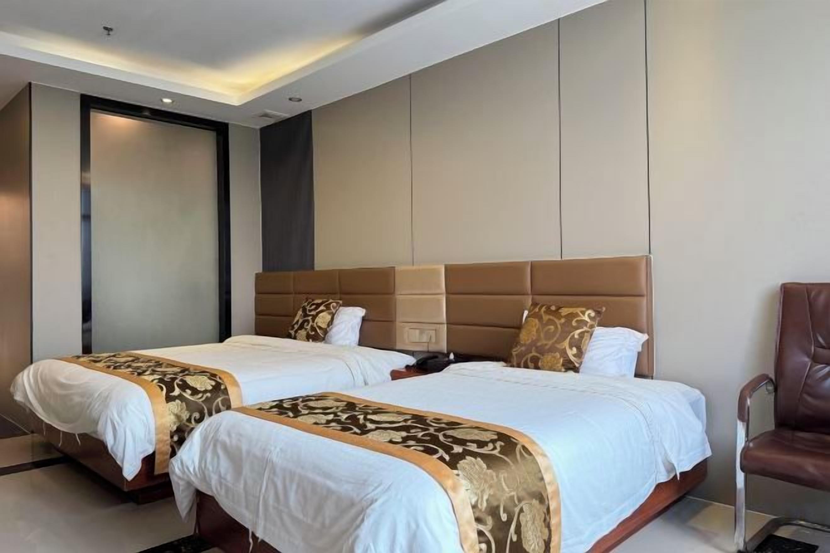 Une chambre d’hôtel avec deux lits, une grande tête de lit et un fauteuil en cuir.
