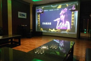 A room with a stage, a screen displaying a performer, and a table with glasses. - Hengshan Hotel (Taishan)