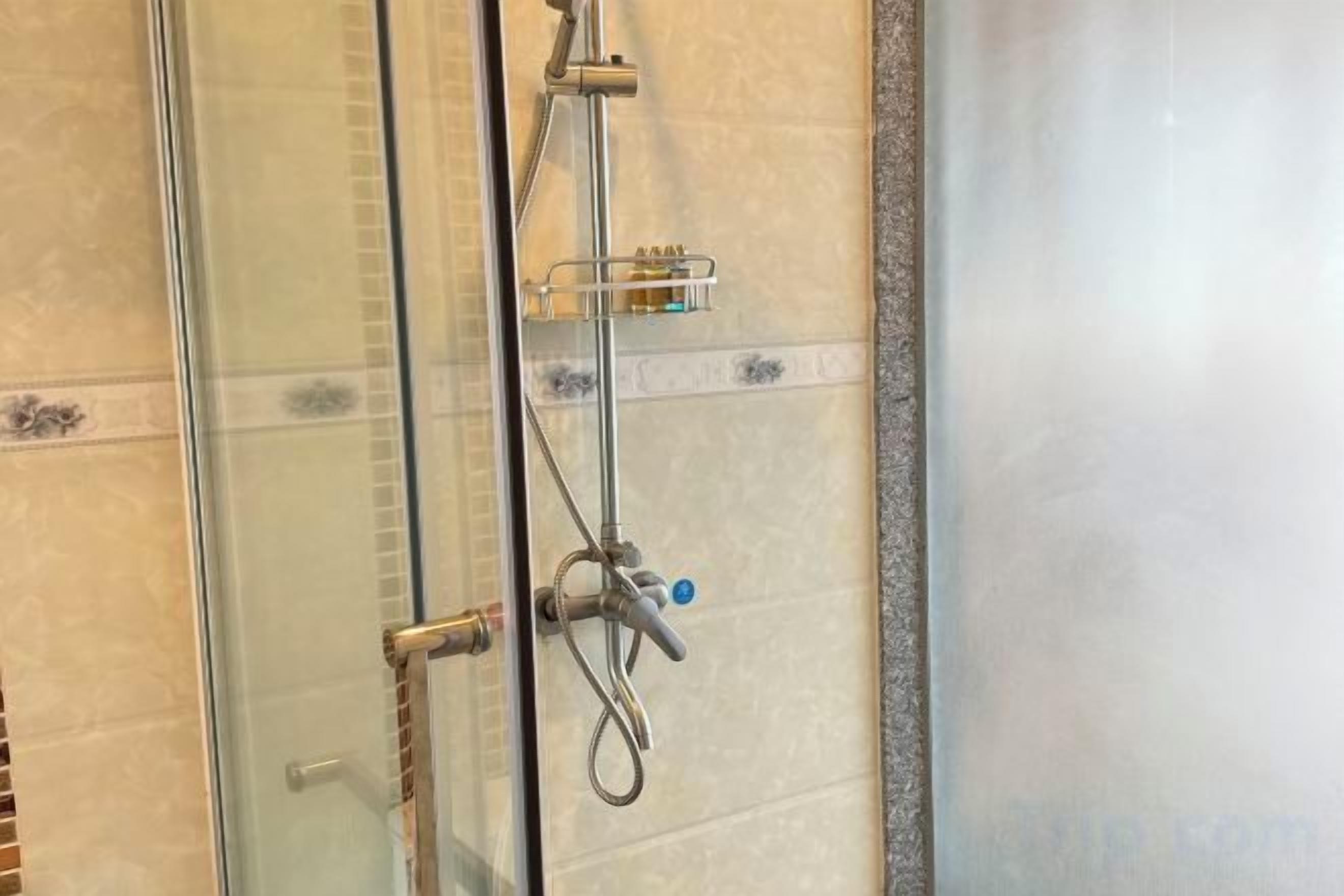 Zona de ducha con mampara de vidrio, cabezal de ducha de mano y llave de pared.