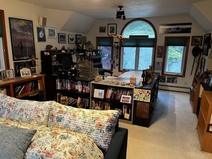 A cozy living room with a large window, a bookshelf filled with books, and a floral-patterned couch.