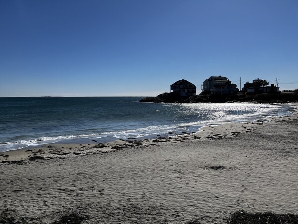 A beach with a rocky outcrop and houses in the background.