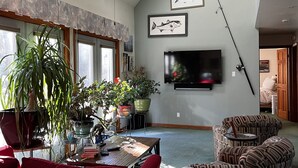 Un salon spacieux doté d’un ventilateur de plafond, d’un téléviseur à écran plat fixé au mur et de plusieurs plantes en pot.