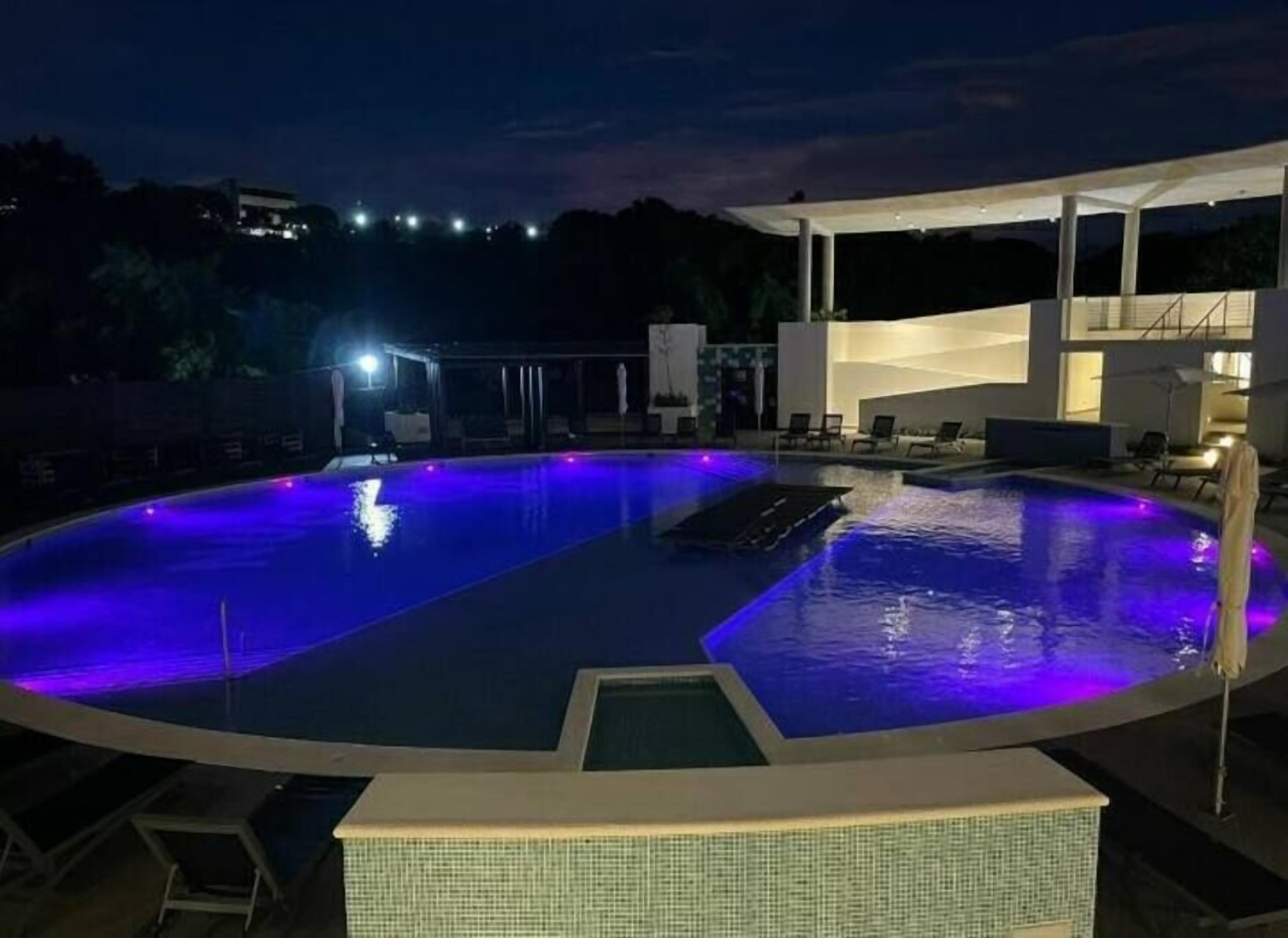 A swimming pool with a modern design, surrounded by lounge chairs and a covered area with seating.