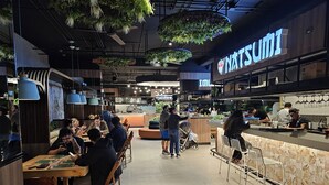 Et moderne restaurantmiljø med træborde og -stole, et barområde og hængende planter.