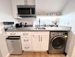 Eine kompakte Küche mit Mikrowelle, Kaffeemaschine, Spüle und Waschmaschine.