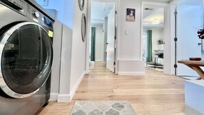 A laundry area with a washing machine, a hallway leading to a dining area, and a kitchen visible in the background. - Garden Retreat | Firepit | 911Mbps | W/D| Smart TV (San Francisco)
