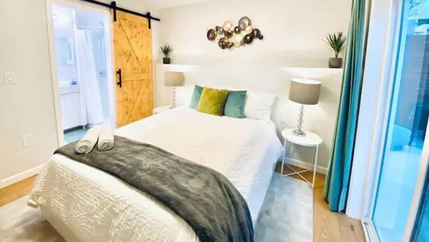 A modern bedroom with a bed, bedside lamps, a sliding door, and a view of the outdoors. - Garden Retreat | Firepit | 911Mbps | W/D| Smart TV (San Francisco)