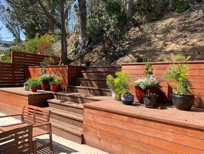 Relax in a serene outdoor seating area surrounded by lush greenery and a hillside backdrop.