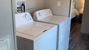Une buanderie équipée de deux machines à laver blanches, d’un panneau de commande et d’une boîte électrique fixée au mur.