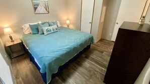 Une chambre à coucher avec un lit, deux lampes de chevet, une porte et une petite table sur laquelle est posée une plante.