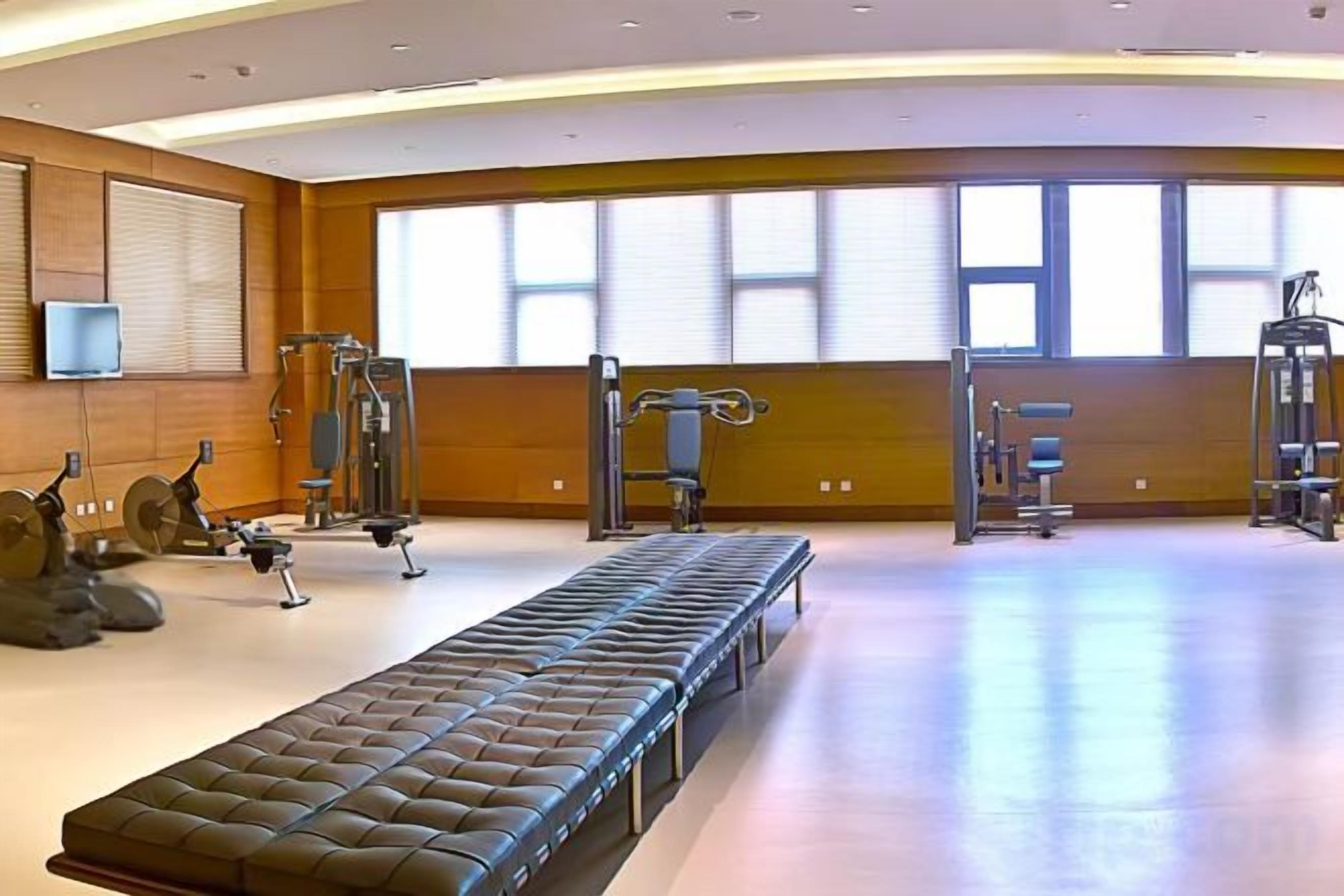 Une salle de sport spacieuse, équipée de matériel d’exercice, d’un banc et de grandes fenêtres.