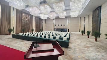 A large hall with a stage, rows of chairs, a podium, and decorative lighting.