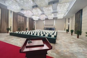 A large hall with a stage, rows of chairs, a podium, and decorative lighting.