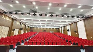 Un ampio auditorium con file di poltrone rosse, un palco con un leggio e un soffitto con più luci.