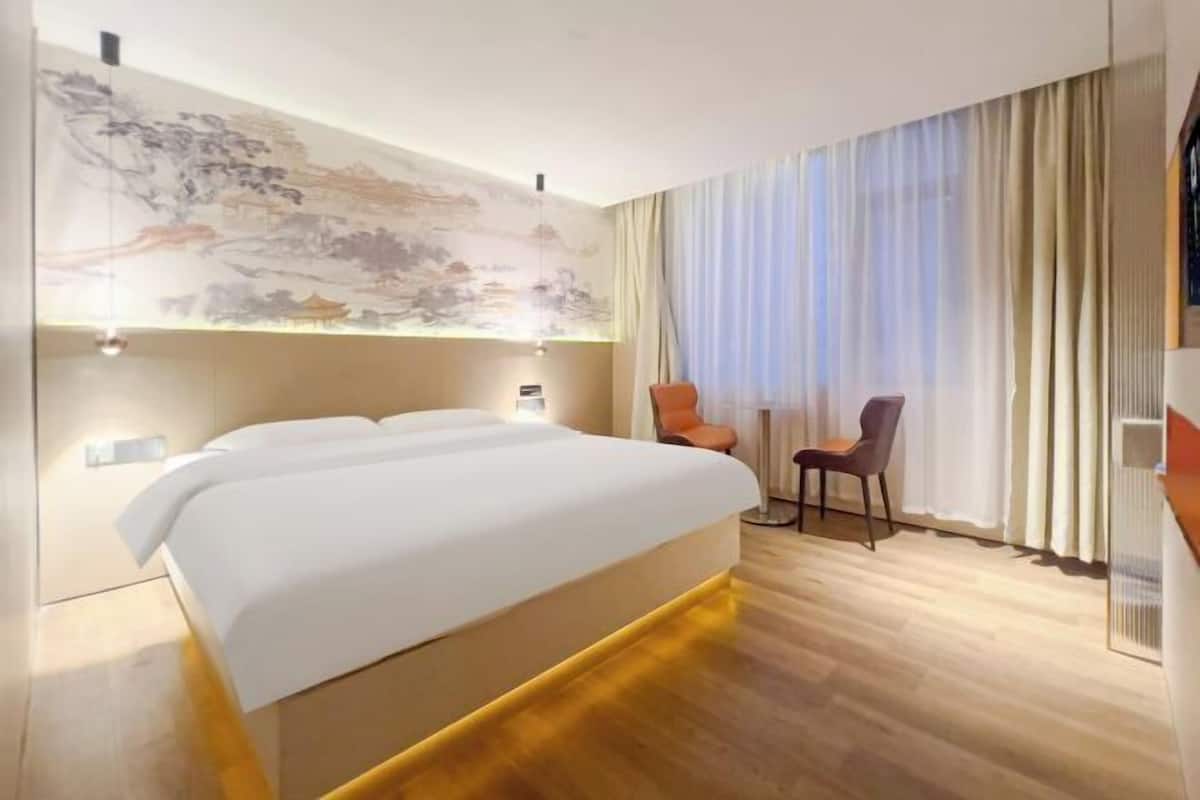 A modern hotel room with a large bed, two chairs, a large window with curtains, and a wall mural.