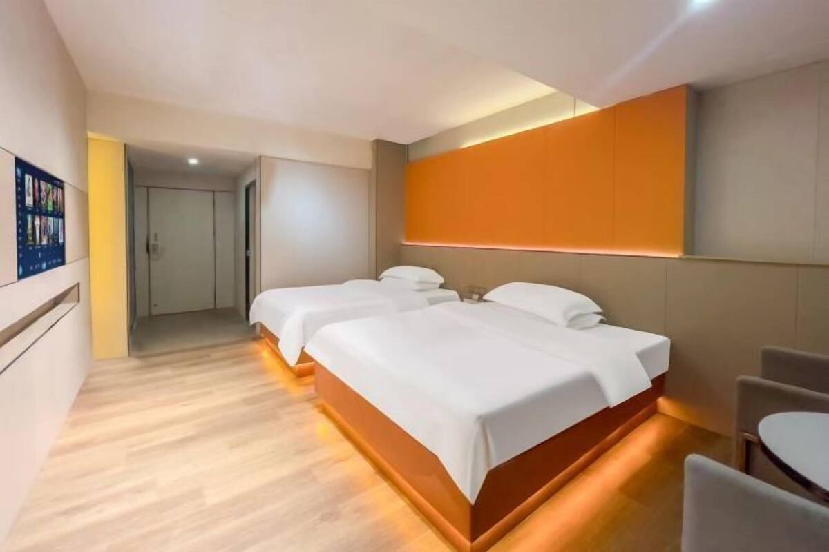 A hotel room with two beds, a small table, and a wall-mounted TV.