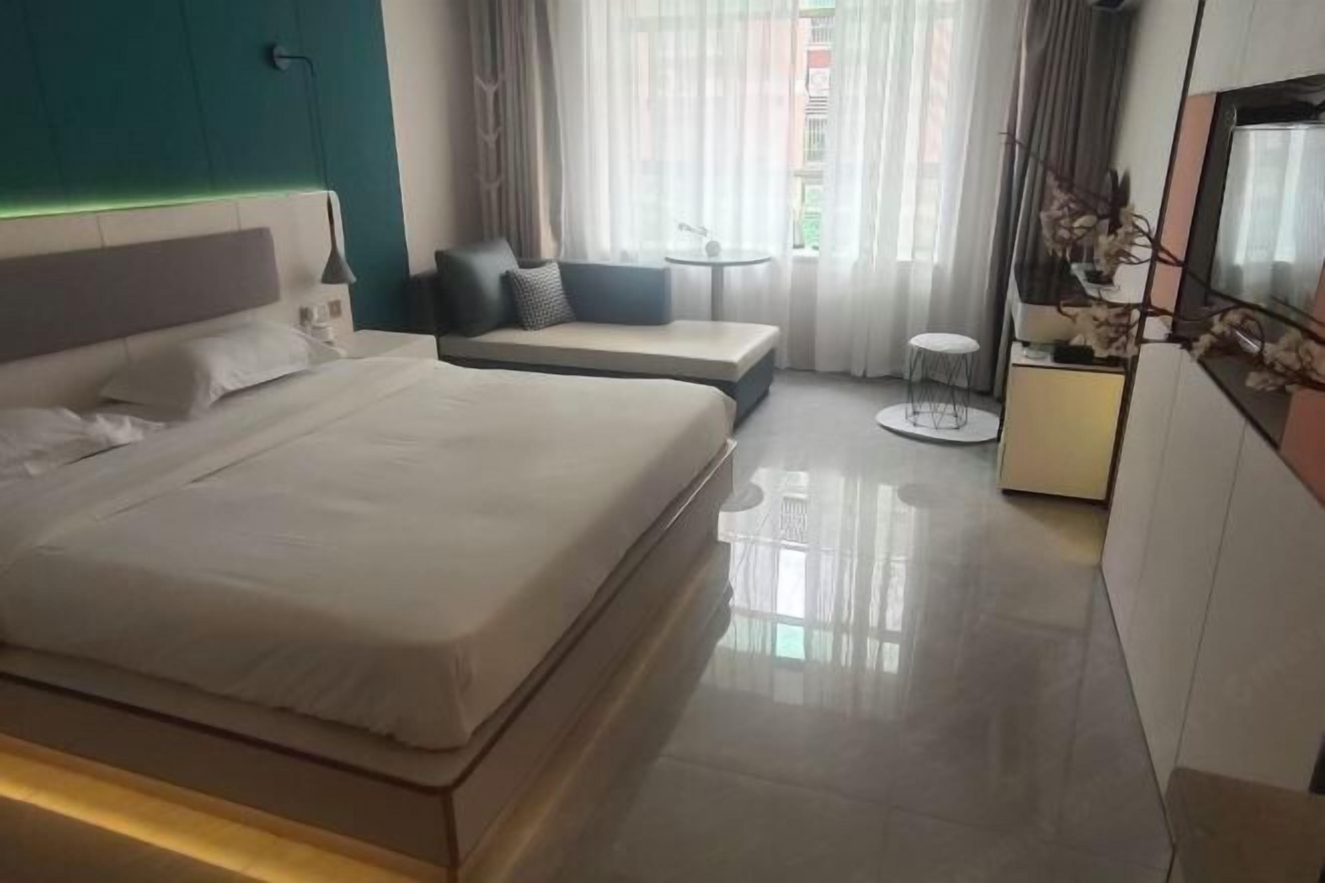 Quarto de hotel moderno com uma cama grande, um sofá, uma mesinha e uma televisão.