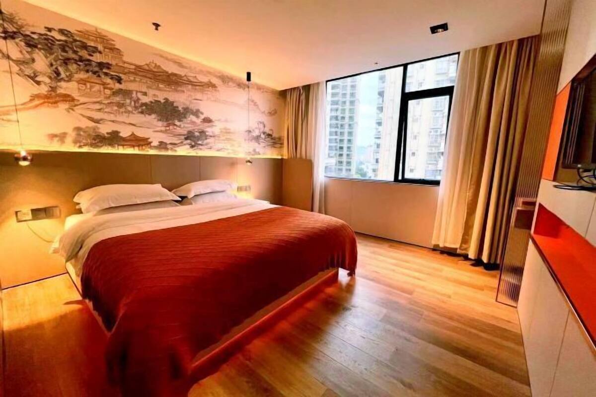 A modern hotel room with a large bed, a painting on the wall, a window with curtains, and a TV on the right side.