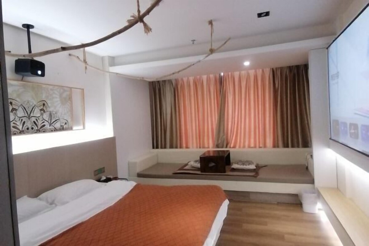 A modern hotel room with a bed, a seating area with a laptop, and a large window with curtains.