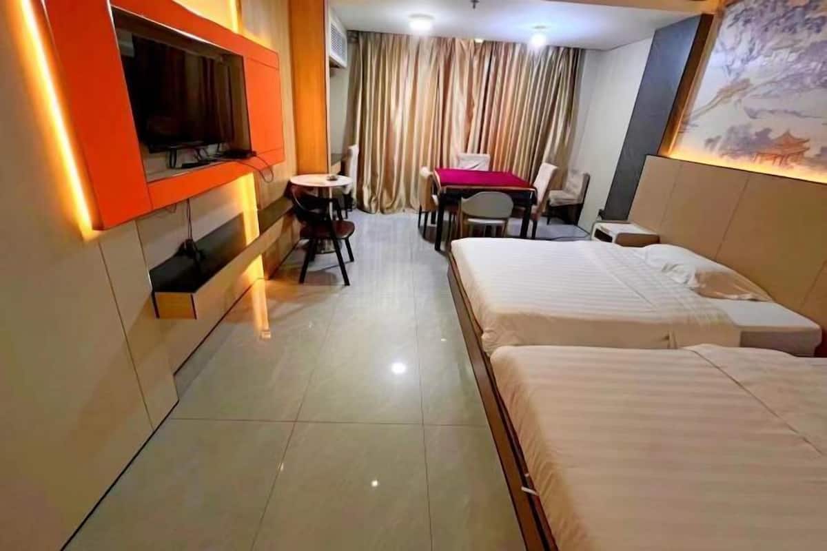 A hotel room with two beds, a TV mounted on the wall, a small table with chairs, and a curtain-covered window.