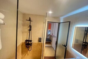 A modern bathroom with a glass shower enclosure, a towel rack, and a visible kitchen area in the background. - Fan She Fashion Hotel (Heyuan)