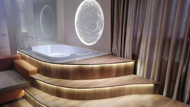 A modern bathroom with a curved wooden vanity, a bathtub, and a moon projection on the wall. - Fan She Fashion Hotel (Heyuan)