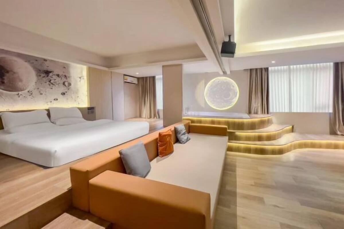 A modern hotel room with a bed, sofa, and a unique circular light fixture.