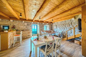 Un intérieur rustique avec un mur en pierre, des poutres en bois au plafond, un coin repas avec des meubles blancs et une cheminée en pierre.