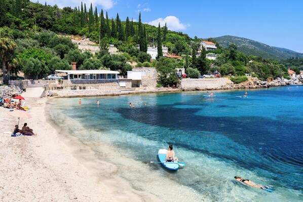 A coastal area with clear waters, a sandy beach, and buildings on a hillside.