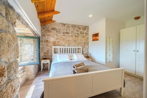 Une chambre avec un mur en pierre, un cadre de lit en bois, une table de chevet, une armoire et une fenêtre donnant sur un beau paysage.