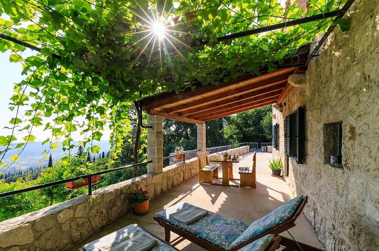 A covered outdoor seating area with stone walls, a pergola, and a view of the landscape.