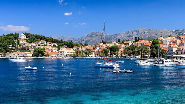 A coastal town with boats docked in the harbor, clear blue water, and buildings with red roofs.