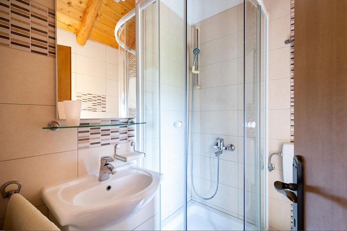 Une salle de bain moderne avec une douche à parois de verre, un lavabo blanc et un mur recouvert de carreaux.