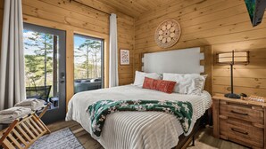A wooden-paneled bedroom with a bed, bedside table, and a view of trees through a door. - "This cabin is absolutely beautiful and in a gorgeous and quiet area!" (Sevierville)