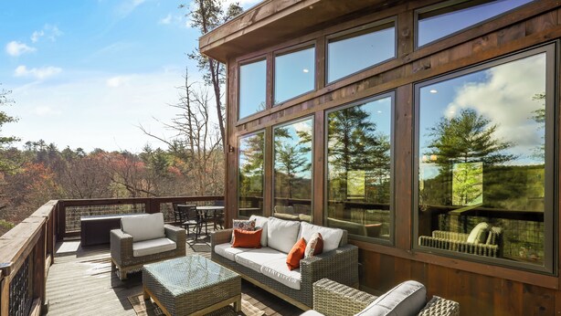 A wooden deck with wicker furniture and large windows overlooking a forested area. - "This cabin is absolutely beautiful and in a gorgeous and quiet area!" (Sevierville)