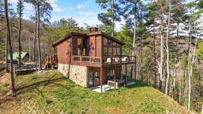 A two-story wooden cabin with a stone foundation, a balcony, and a stone fireplace.