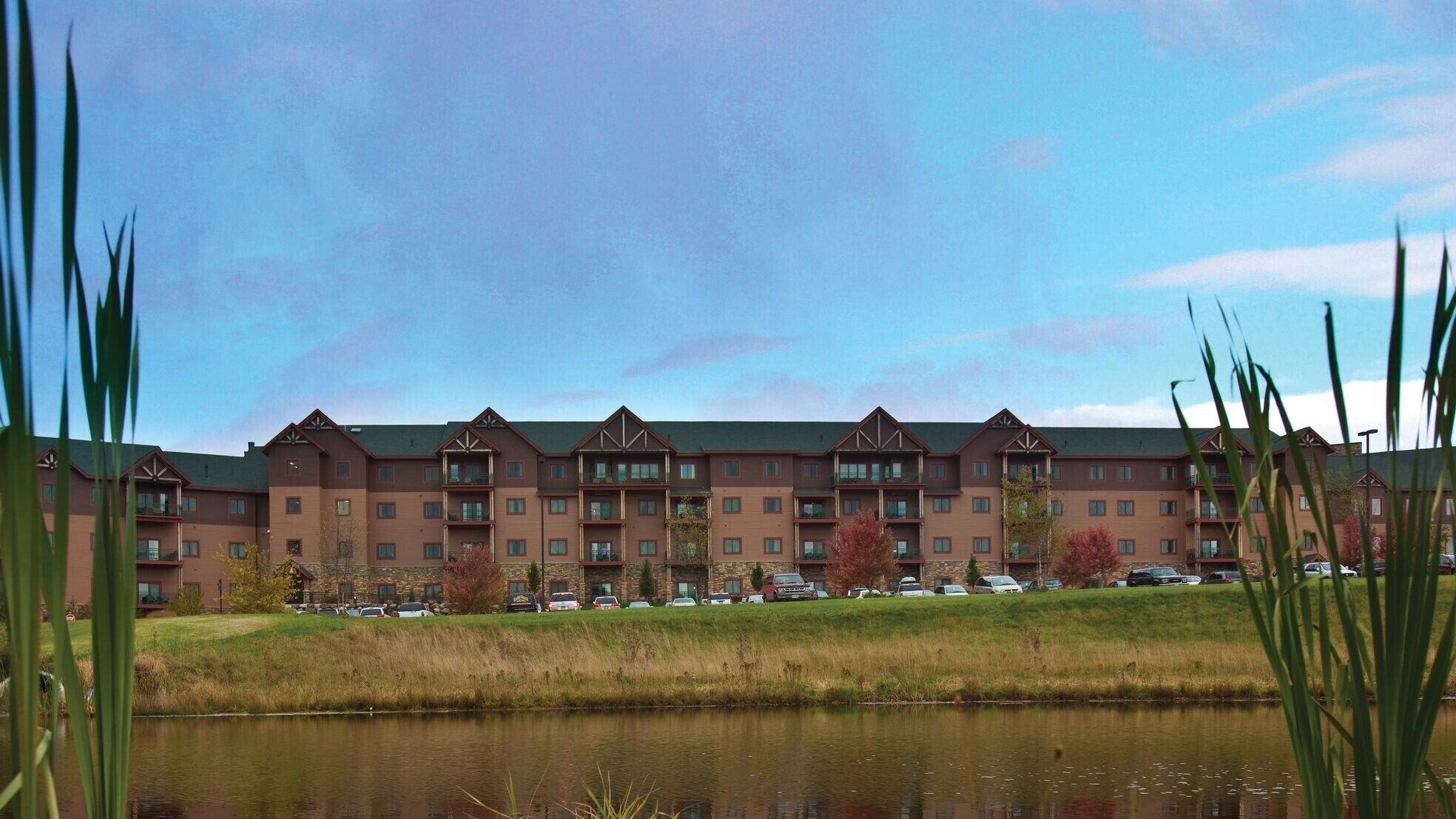 A multi-story hotel with a symmetrical facade, a green lawn, and a body of water in the foreground.
