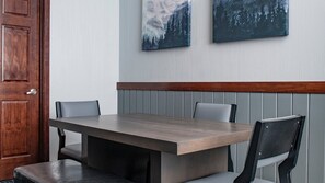 A dining area with a wooden table and chairs, a wooden door, and two framed pictures on the wall.