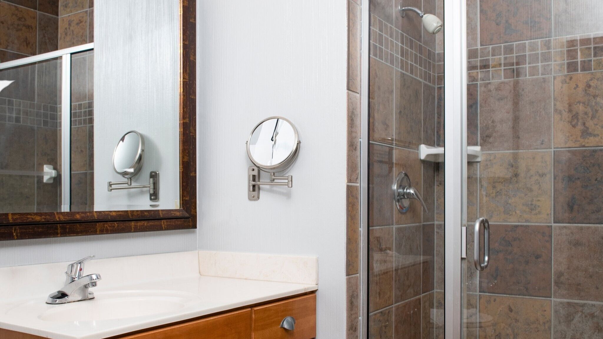A bathroom with a white sink, a mirror, a wall-mounted scale, and a shower with tiled walls.