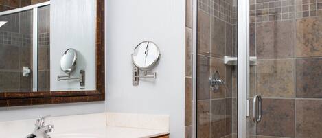 A bathroom with a white sink, a mirror, a wall-mounted scale, and a shower with tiled walls.