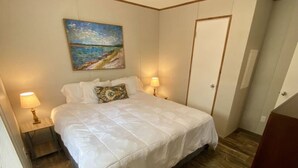 A bedroom with a bed, two bedside lamps, a painting on the wall, and a door. - Rainbow River Bungalow D (Dunnellon)
