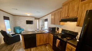 A kitchen with wooden cabinets, a black refrigerator, a stove, and a sink. - Rainbow River Bungalow D (Dunnellon)