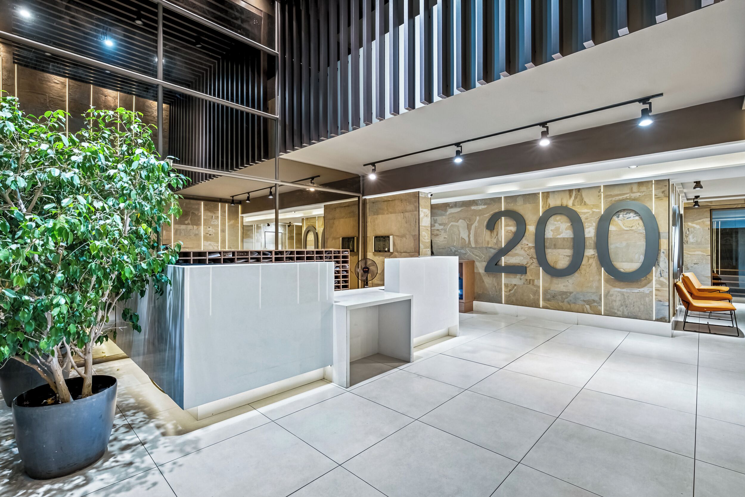 Un espace d’accueil moderne, avec un comptoir de réception, un grand chiffre « 200 » peint sur le mur et une plante en pot.