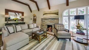 A living room with a stone fireplace, a sofa, a chair, a coffee table, and a bookshelf. - East Dallas 3BR Home with Pool, Spa & Fireplace (Dallas)