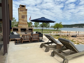 An outdoor patio with a stone fireplace, lounge chairs, and a view of a lake. - Waterfront PK Lake Home with Private Boat Dock (Graford)