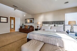 Quarto com cama grande, sofá, mesa de cabeceira e espelho.